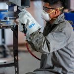 Auto body technician in safety gear working on a steel rail section in the shop