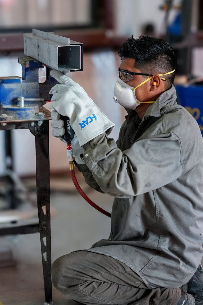 Auto body technician in safety gear working on a steel rail section in the shop